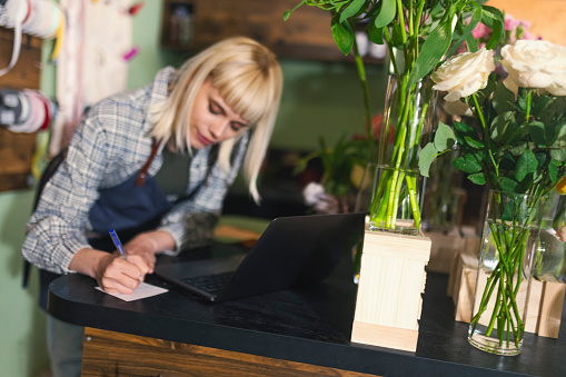 The florist takes inventory in flower shop and writes down on paper what to order from the supplier