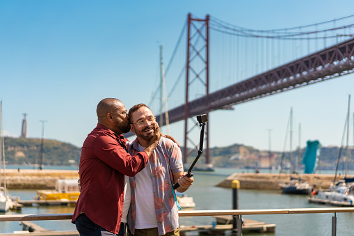 Gay couple taking a selfie in front of the 25 de Abril Bridge