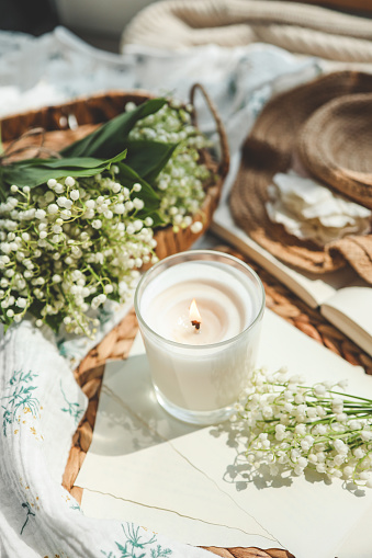 A white burning candle and a bouquet of lilies of the valley, a natural spring photo.