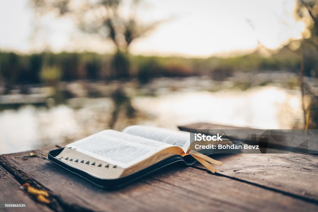 Open Bible on a wooden board near the river Open Bible on a wooden board near the river. Bible Stock Photo
