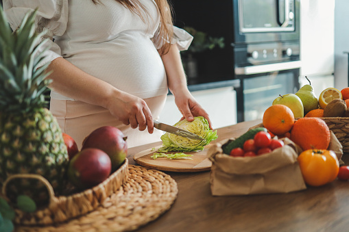 Pregnant woman making salad in her kitchen, healthcare.