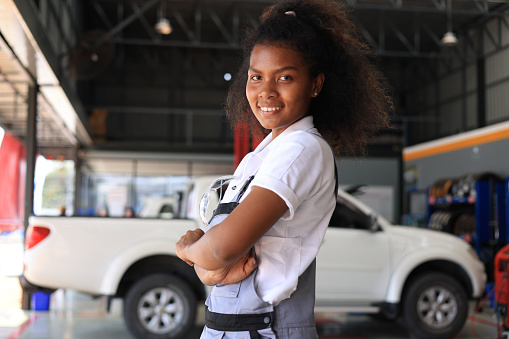 African American female car mechanic crossing her arms and looking at the camera, Portrait of a young african american woman, a professional female mechanic smiling at the camera standing in the auto repair shop. Car service, repair, maintenance, and people concept. Horizontal shot