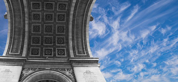 Arc de Triomphe (against the background of sky with clouds), Paris, France. The walls of the arch are engraved with the names of 128 battles and names of 660 French military leaders (in French)