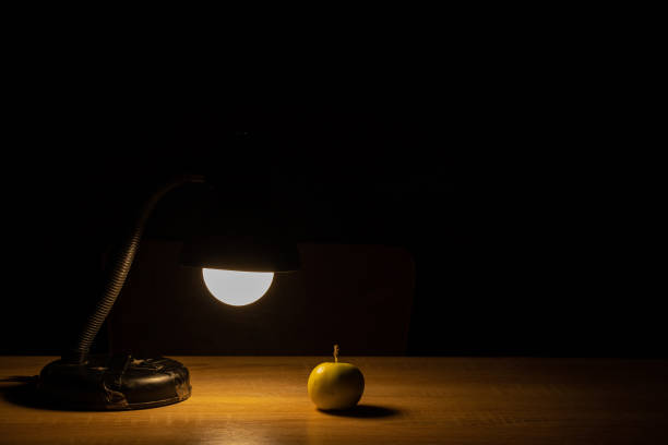 one apple on a table in a dark room and a table lamp illuminates the table
