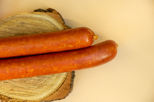 two sausages lie on a round wooden board on a brown background close-up