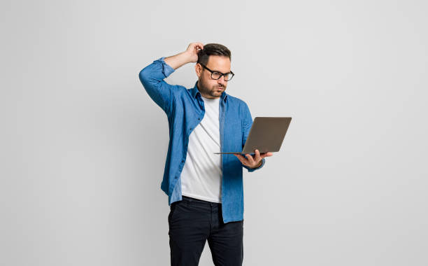 Confused disappointed businessman with hand in hair reading e-mail over laptop on gray background Confused disappointed businessman with hand in hair reading e-mail over laptop on gray background worried man standing stock pictures, royalty-free photos & images