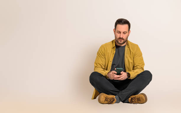 istock Serious young handsome businessman reading text messages on smart phone while sitting with legs crossed. Male professional dressed in casuals checking social media on cellphone against background 1505972055