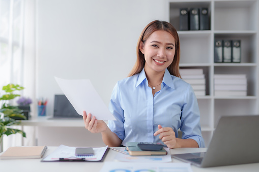 Beautiful young business woman manager or company worker holding accounting document, checking financial data or marketing report working in office with laptop. Accountant consults on some docum