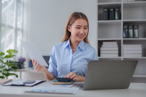Beautiful young business woman manager or company worker holding accounting document, checking financial data or marketing report working in office with laptop. Accountant consults on some docum