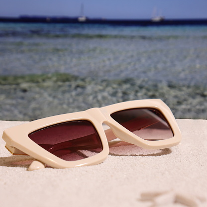 Beige fashion sunglasses on sand, summer accessories on the beach