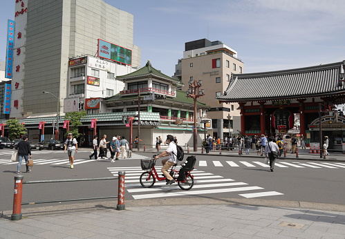 Taito Ward, Japan - May 28, 2023: Cyclists and pedestrians share the scramble crossing on Kaminarimon-dori Street outside Kaminarimon Gate with the red lantern. Looking northwest in Asakusa district on a spring morning.