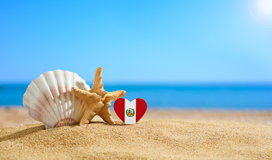 Flag of Peru in the shape of a heart and seashells on a sandy beach