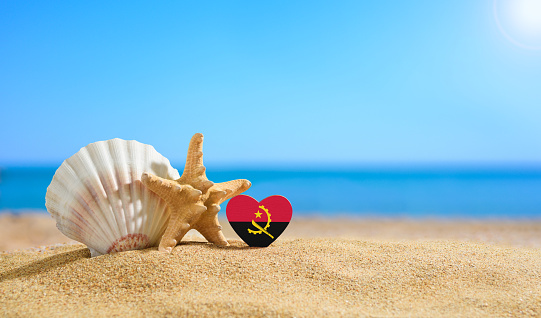 Beautiful beach in Angola. Flag of Angola in the shape of a heart and shells on a sandy beach.