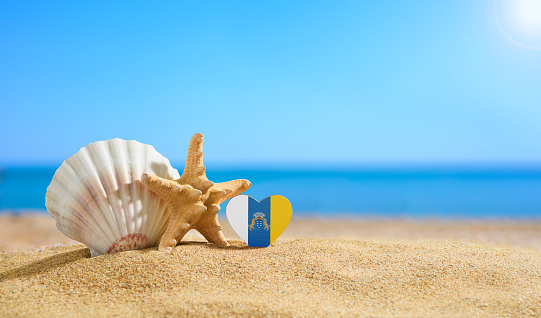 Beautiful beach in the Canary Islands. Flag of Canary Islands in the shape of a heart and shells on a sandy beach.