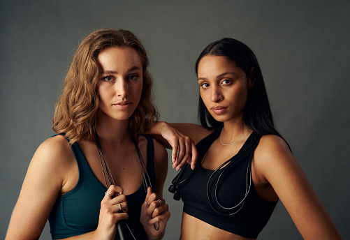 Young woman wearing sports bra holding jump rope while looking at camera with friend