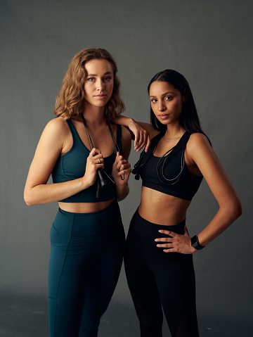 Determined young woman wearing sports bra holding jump rope while looking at camera with friend