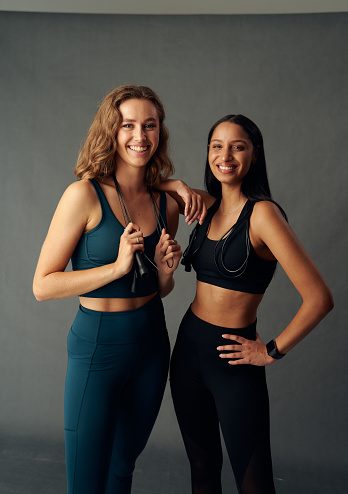Happy young woman wearing sports bra holding jump rope while looking at camera with friend