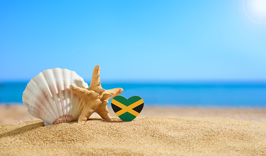 Beautiful beach in the Jamaica. Flag of Jamaica in the shape of a heart and shells on a sandy beach.