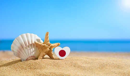 Beautiful beach of Japan. Flag of Japan in the shape of a heart and shells on a sandy beach.