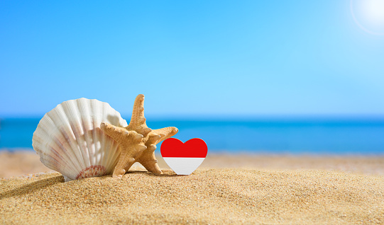 Beautiful Indonesian beach. Flag of Indonesia in the shape of a heart and shells on a sandy beach.
