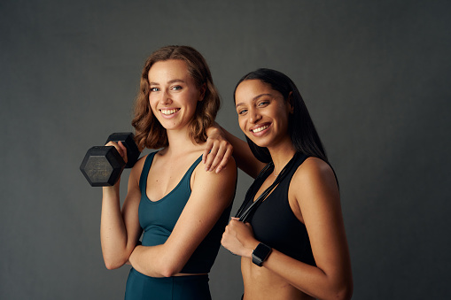 Happy young women wearing sports bra smiling while looking at camera and holding exercise equipment