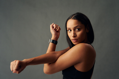Portrait of young biracial woman wearing sports bra looking away while doing cross arm stretch in studio