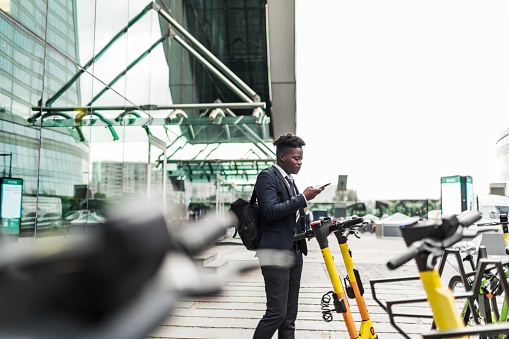 Young adult black businessman renting electric scooter using mobile app