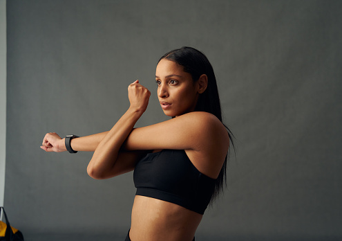 Determined young biracial woman wearing sports bra doing cross arm stretch in studio