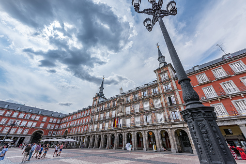 Madrid, Spain - June 20, 2023: Tourist and local residents are walking on Plaza Mayor in Madrid. The Plaza Mayor is currently an important tourist spot, visited by thousands of tourists a year. In the commercial premises located under the arcades, catering businesses abound, which set up terraces next to the arcades of the square.