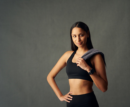 Young biracial woman wearing sports bra and fitness tracker looking away while holding towel in studio