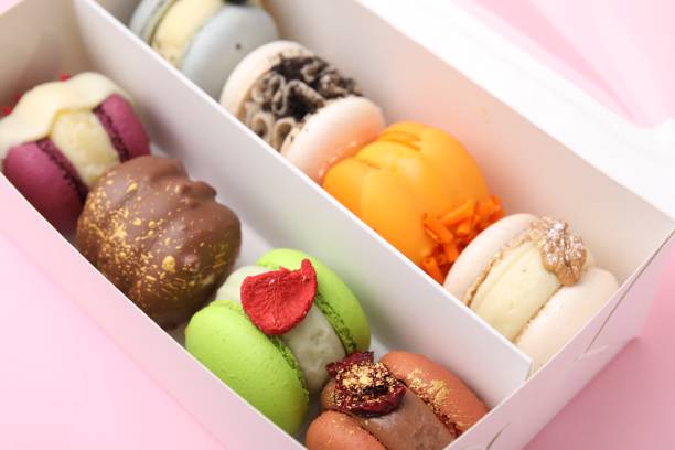 istock Cardboard box with delicious macarons on pink table, closeup 1506159886