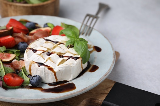 Plate of delicious salad with brie cheese, berries and balsamic vinegar on light grey table, closeup. Space for text