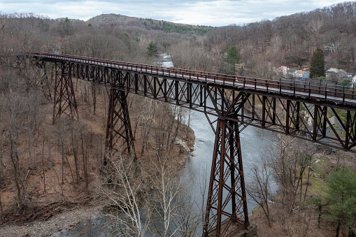 A set of curved railroad tracks slanted toward the inside of the curve atop a gravel railroad bed and railroad ties in a forested area on a sunny day.