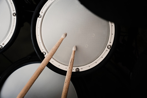 Top view of electronic drum kit with cymbals and drums and a pair of wooden drumsticks, on a black background. Percussion instrument concept.