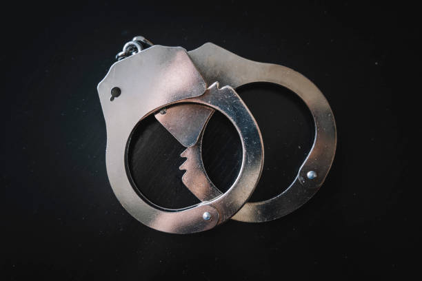 concept of arrest and crime. metal handcuffs on a black table background the concept of arrest and crime. metal handcuffs on a black table background white collar crime handcuffs stock pictures, royalty-free photos & images
