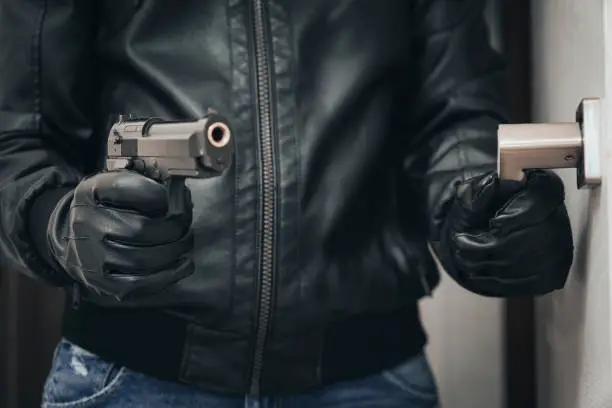 bank robbery. an armed criminal with a dhrt pistol enters the premises. Attempted robbery. Crime concept. self-defense with firearms. the man hides the gun behind his back.