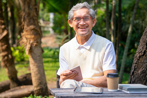 healthy asian senior man siting in the summer park,older adult enjoy leisure time relaxing,reading,chatting internet online smartphone in garden,concept old people lifestyle,health benefits in nature