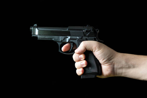 mano che tiene una pistola, su sfondo nero. concetto del crimine di banditismo. un tiratore pericoloso e una pistola nera su uno sfondo scuro. il killer assoldato si prepara a sparare. - gun gunman handgun men foto e immagini stock