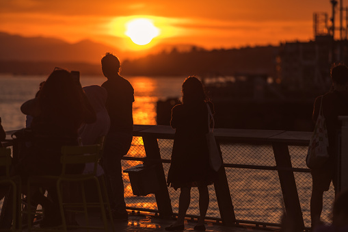 Seattle, USA - Jun 7, 2023: Late in the day a vivid sunset over Elliott bay with people enjoying the view from pier 62.
