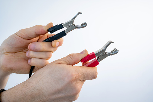 Hands holding crocodile alligator clips red and black color for electrical and electronic testing connect solder. Person measuring of tension and voltage