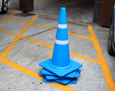 Blue plastic traffic cone on street and painted yellow line surface of street for no parking car.