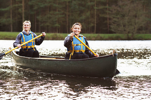 mujeres rowing canoe on aún lago - canoeing fotografías e imágenes de stock