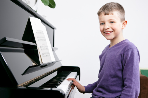 Beautiful little kid boy playing piano in living room or music school. Preschool child having fun with learning to play music instrument. Education, skills concept.