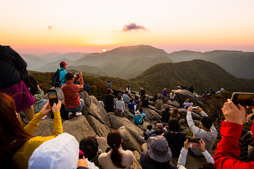 A large group of non recognizable people on top of a mountain watching and taking photos of a sunset across the mountains in central Japan.