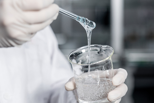 Close-up of a lab technician pouring solution from test tube into a glass flask in laboratory. Scientist working with chemicals for research in a lab.