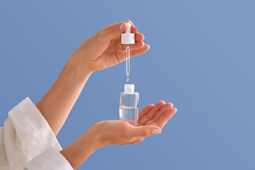 Serum with a pipette in female hands on a bright blue background.
