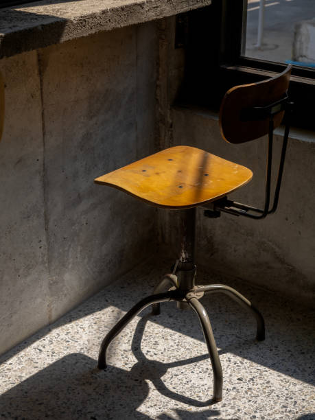 Empty vintage spinning chairs backrest, round seat decorated on concrete wall background, loft style building interior. Swivel wood chair, mid century fashion, wooden and black iron materials.