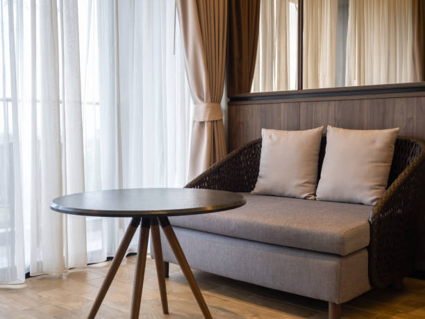 istock Empty modern brown cozy sofa seat made by wicker and grey cushion with two pillows, empty round side table decoration on wood floor near the glass sliding door with white curtains in hotel room. 1506494930