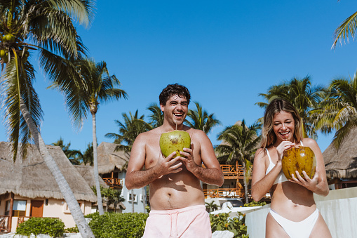 Hispanic young couple holding a coconut and having fun on caribbean beach in holidays or vacations in Mexico Latin America