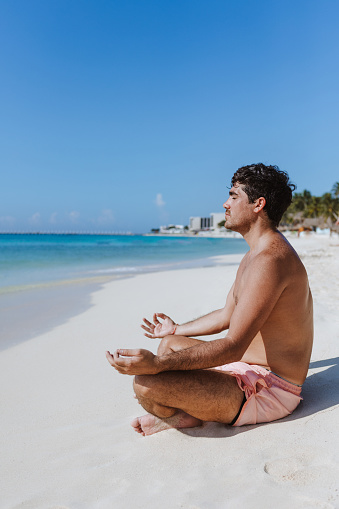 young latin man meditating and relaxation time on the beach in Mexico Latin America, Caribbean and tropical destination